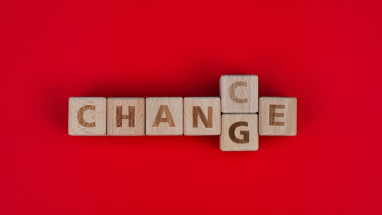 1292721160 Das Bild zeigt Holzbuchstaben auf einem roten Hintergrund, die ein Kreuzworträtsel bilden: Das Wort „CHANGE“ verläuft horizontal, während das Wort „CHANCE“ vertikal dasselbe „C“ wie „CHANGE“ nutzt. Die Komposition hebt die Verbindung zwischen den Wörtern “Veränderung” und “Chance” hervor.